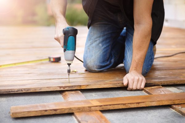 Handyman installing wooden flooring in patio, working with drilling machine